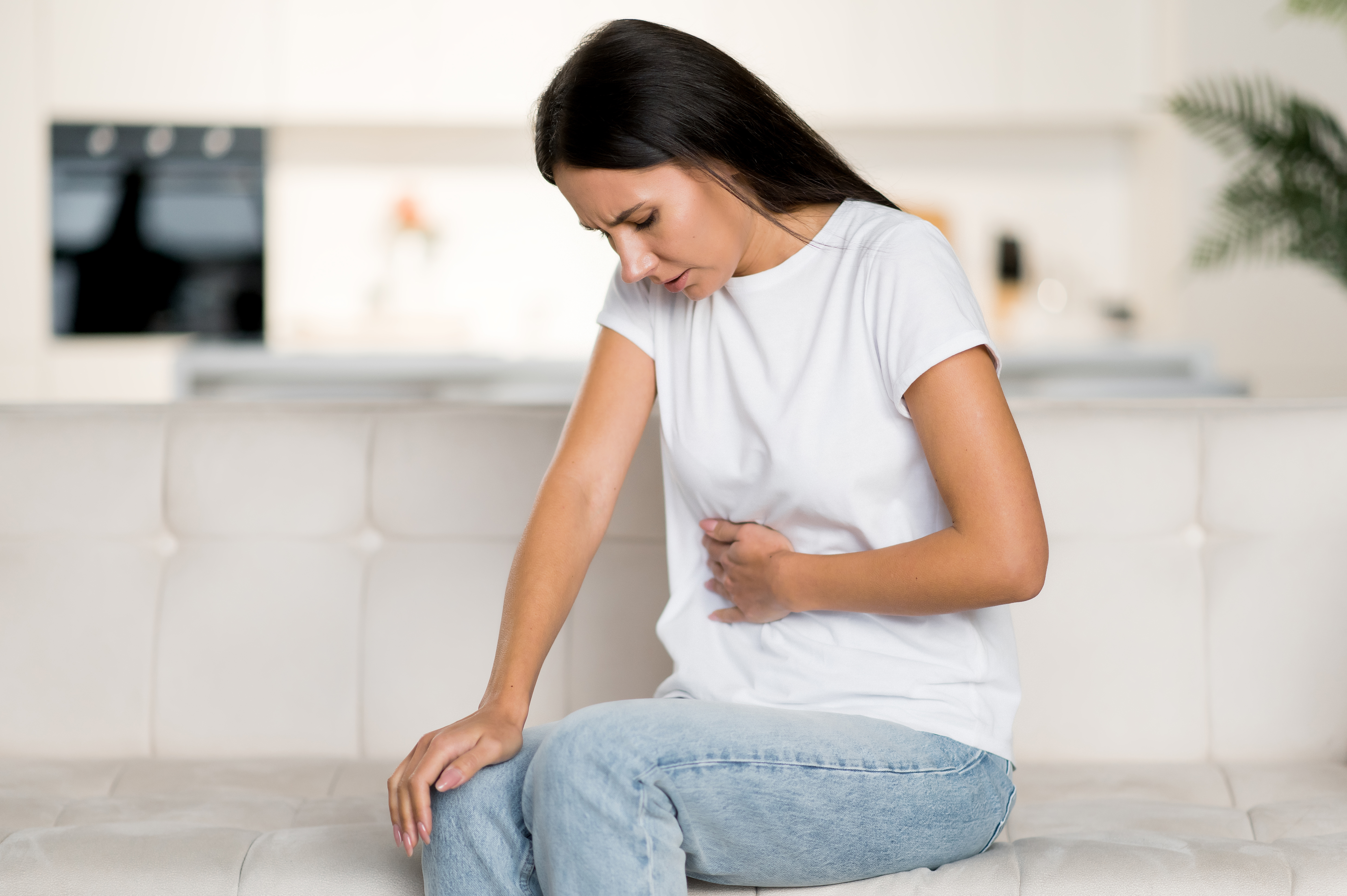 frustrated young caucasian woman, sitting on the sofa in the living room, experiencing abdominal pain, health problems, cramps, ulcer, problems with the digestive tract, need a doctor's consultation